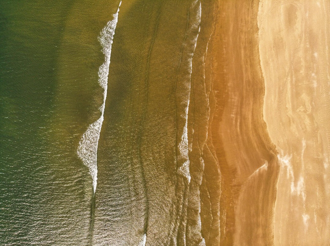 Aerial view of a golden ocean coastline at sunset with waves meeting the shore